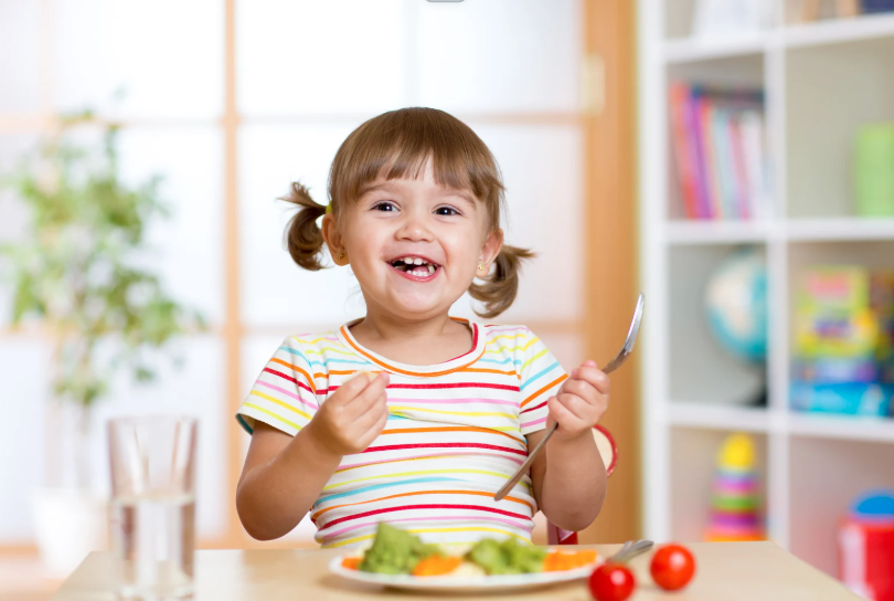 Child happily eating fruit with cutlery